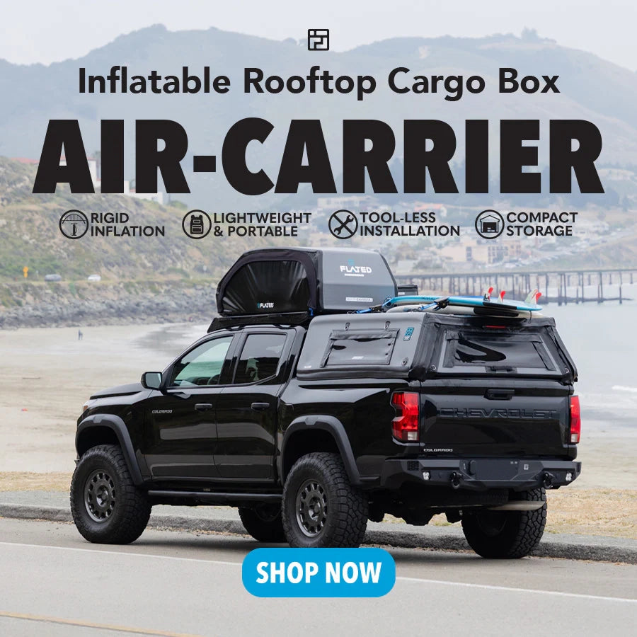 Black truck with inflatable rooftop cargo box on a scenic road.